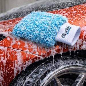 Blue microfiber wash mitt resting on a soapy Ferrari during a foam wash at Carsmotology.