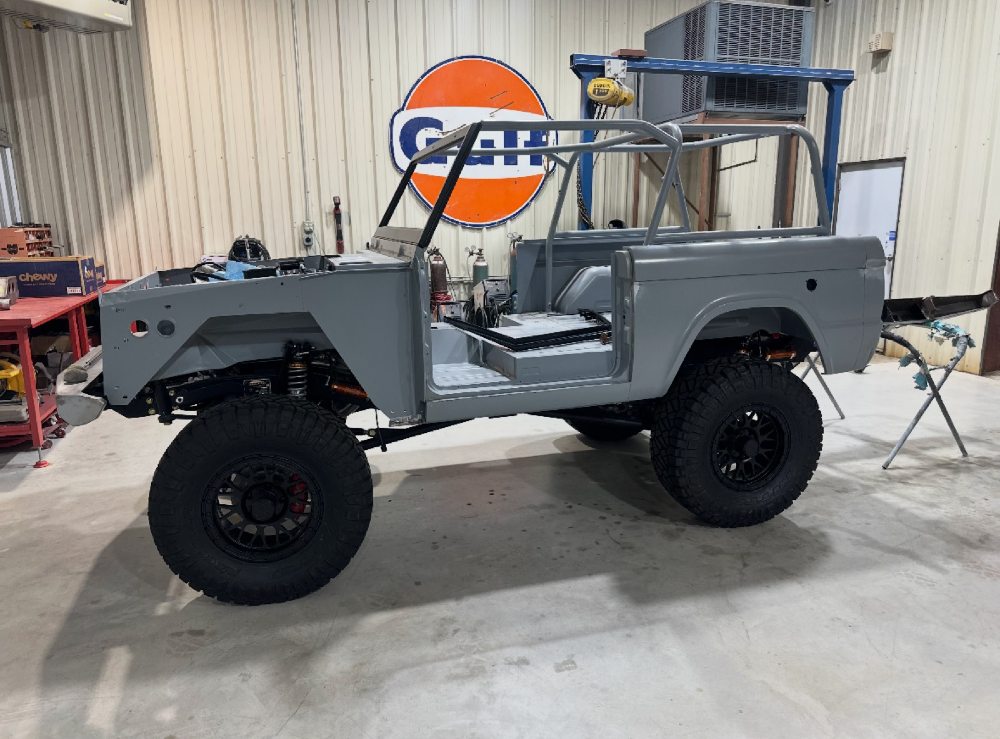Custom Ford Bronco body in gray primer sitting on lifted off-road wheels during the restoration