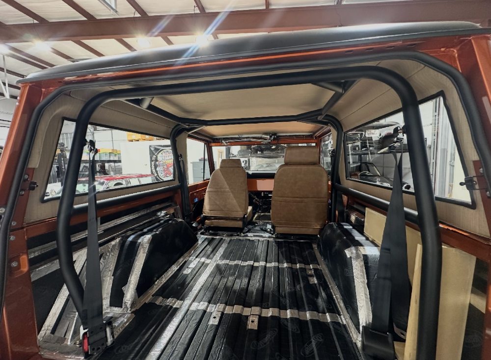 Custom Bronco interior during the build showing a satin-black roll cage and body-color orange dash