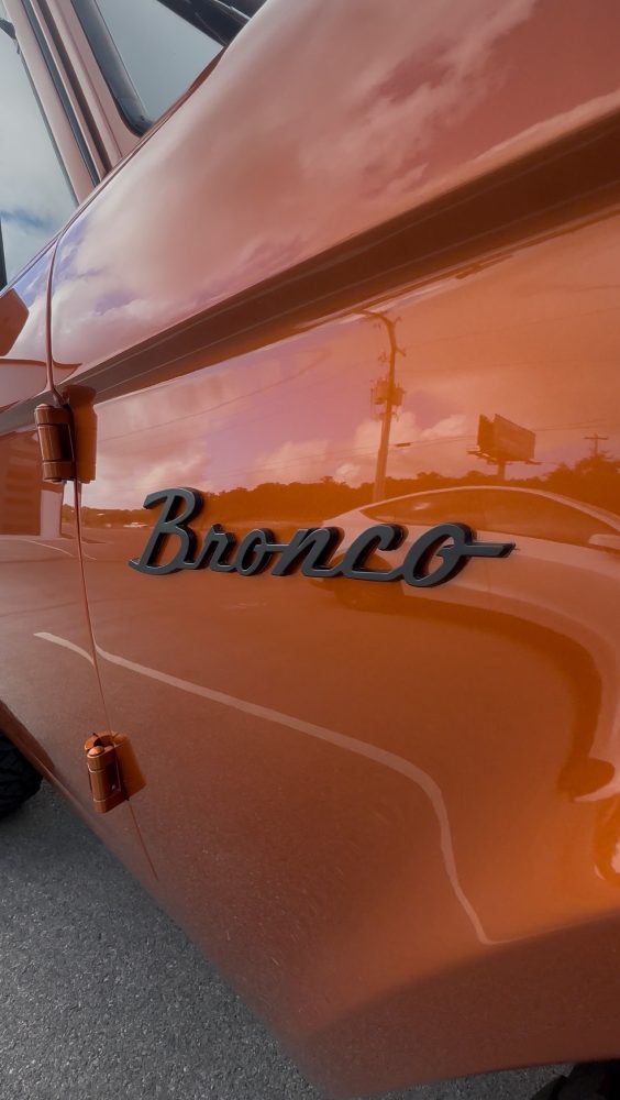 Deep metallic burnt-orange rear quarter panel of the custom Bronco with mirror-like gloss and a Bronco script emblem