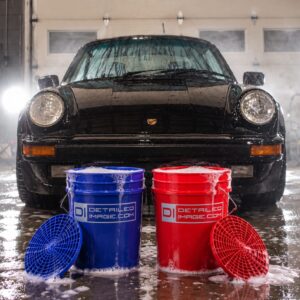 Red and blue Detailed Image wash buckets with grit guards in front of a foamed-up black Porsche