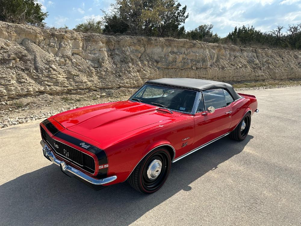 Sunlit front side 1967 Chevrolet Camaro SS/RS convertible detailed by Carsmotology with glossy red paint and black top
