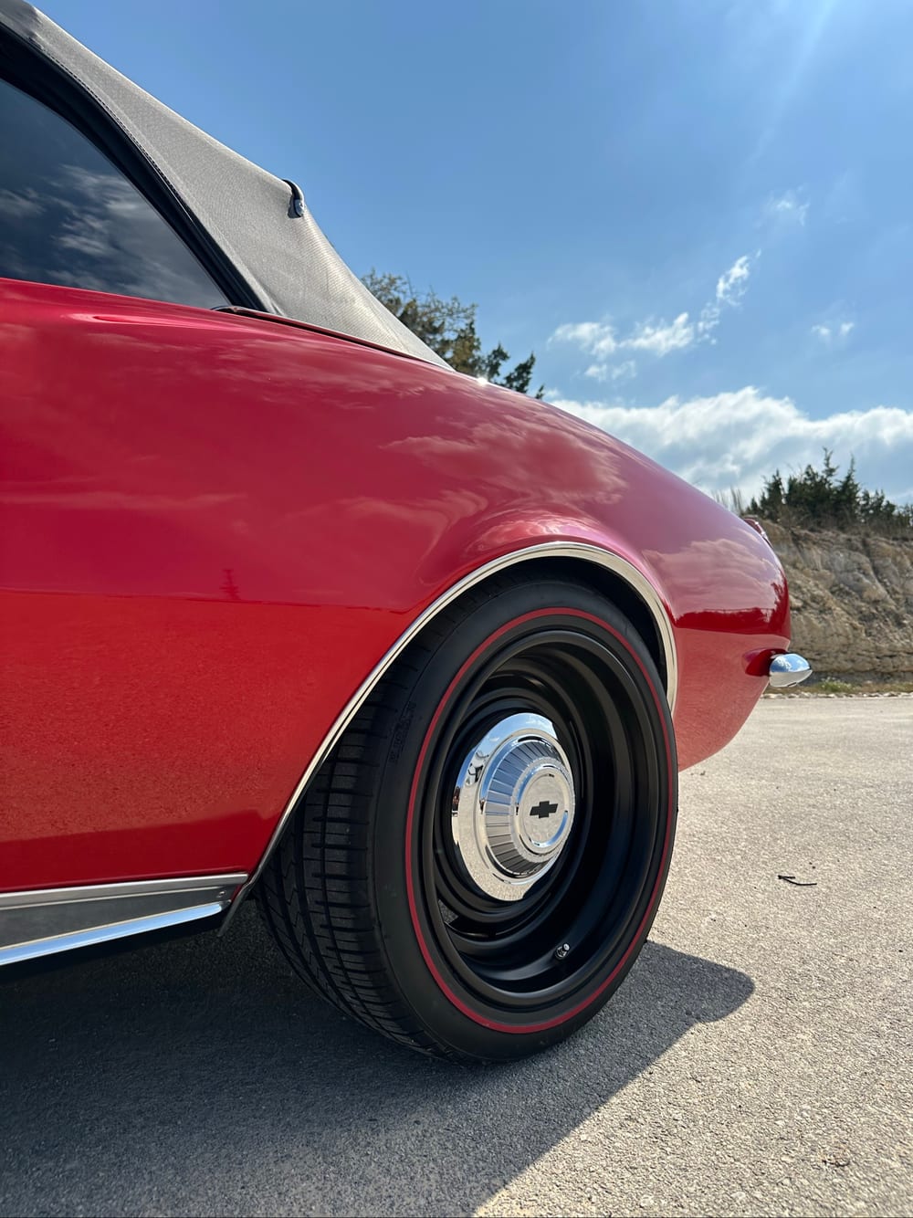 Black steel wheel with a redline tire and chrome Chevy cap on a glossy red 1967 Camaro fender, ceramic coated by Carsmotology