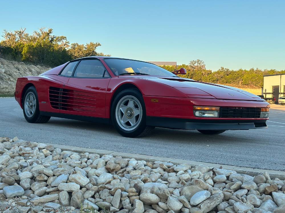 Red Ferrari Testarossa front three-quarter parked near white river rock after paint correction and ceramic coating by Carsmotology