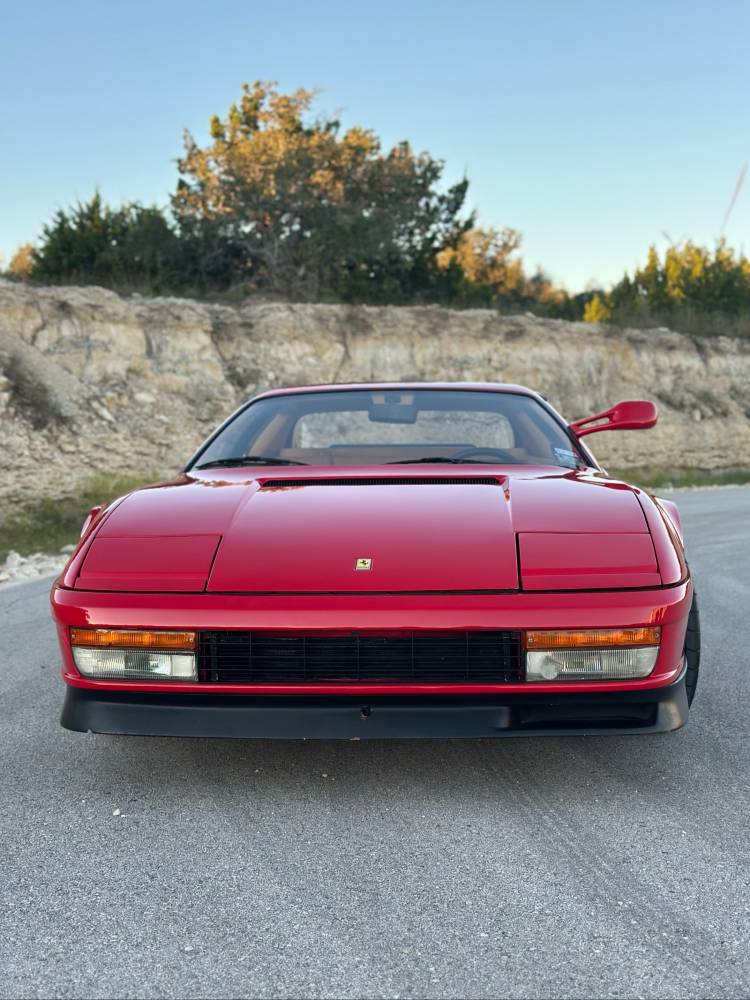 Head-on front view of a red Ferrari Testarossa with pop-up headlights down and the Ferrari shield on the nose, glossy after ceramic coating