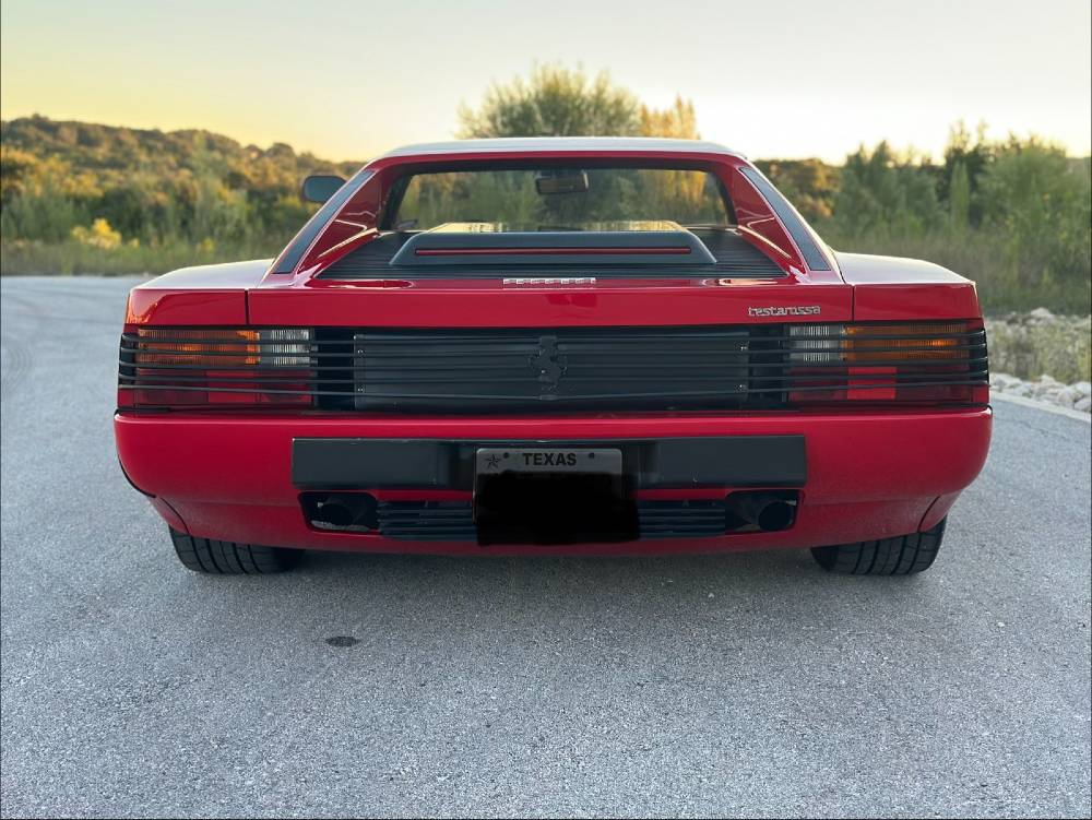 Rear three-quarter of a red Ferrari Testarossa with glossy paint and tail louvers glowing in golden-hour light after ceramic coating