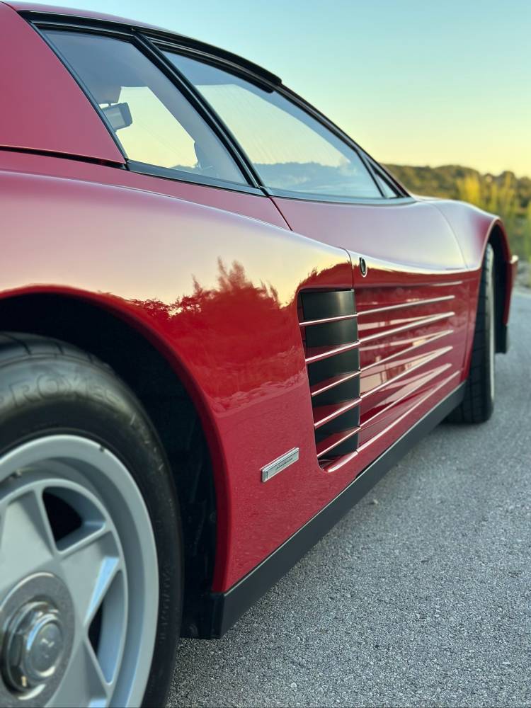 Close-up of a Ferrari Testarossa rear side strake and quarter panel showing mirror-clear reflections after paint correction and ceramic coating